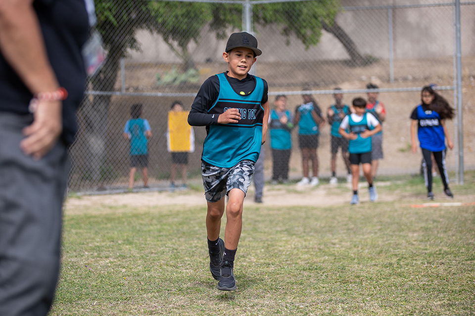 A boy in a teal jersey runs across the field
