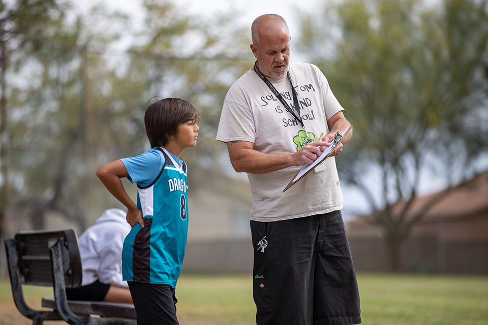 A man with a clipboard points out stats to a boy in a teal jersey