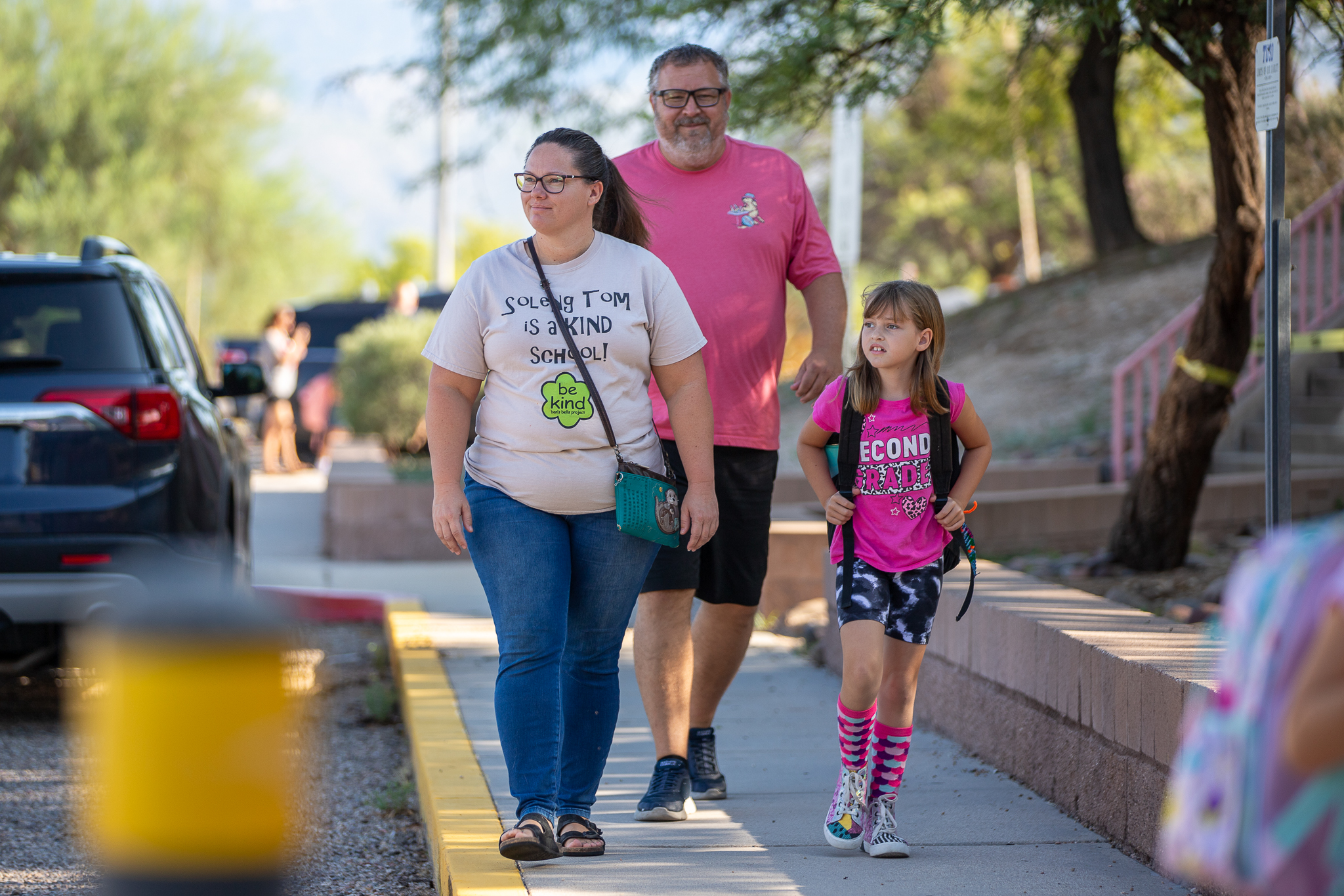 A girl in a pink shirt walks to school with her mom and dad behind her