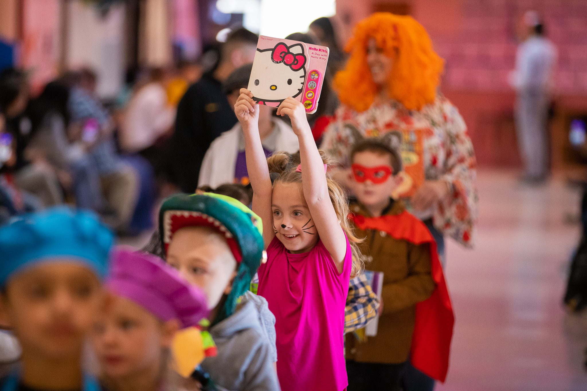 A girl holds up her Hello Kitty book during a Halloween costume parade