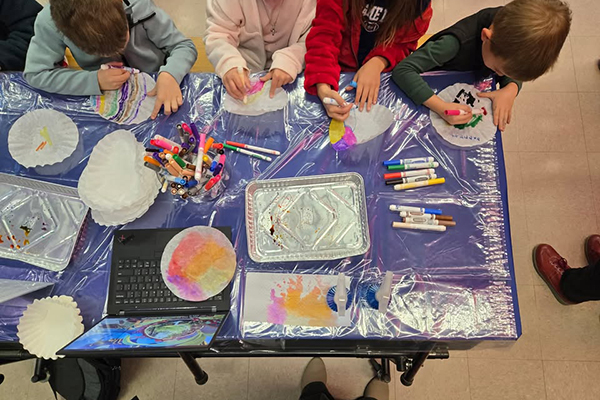Students sitting at a table draw on coffee filters