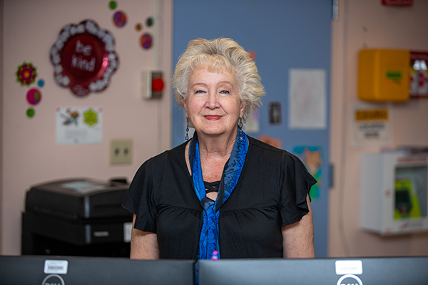 A woman in a black top and blue scarf smiles behind the front desk