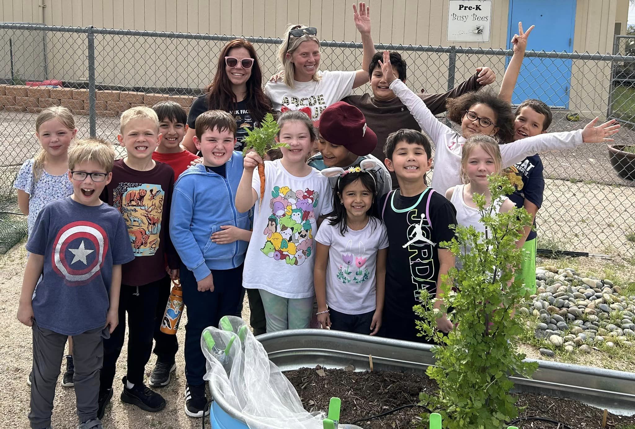 Students proudly hold up the first carrot they grew in their garden